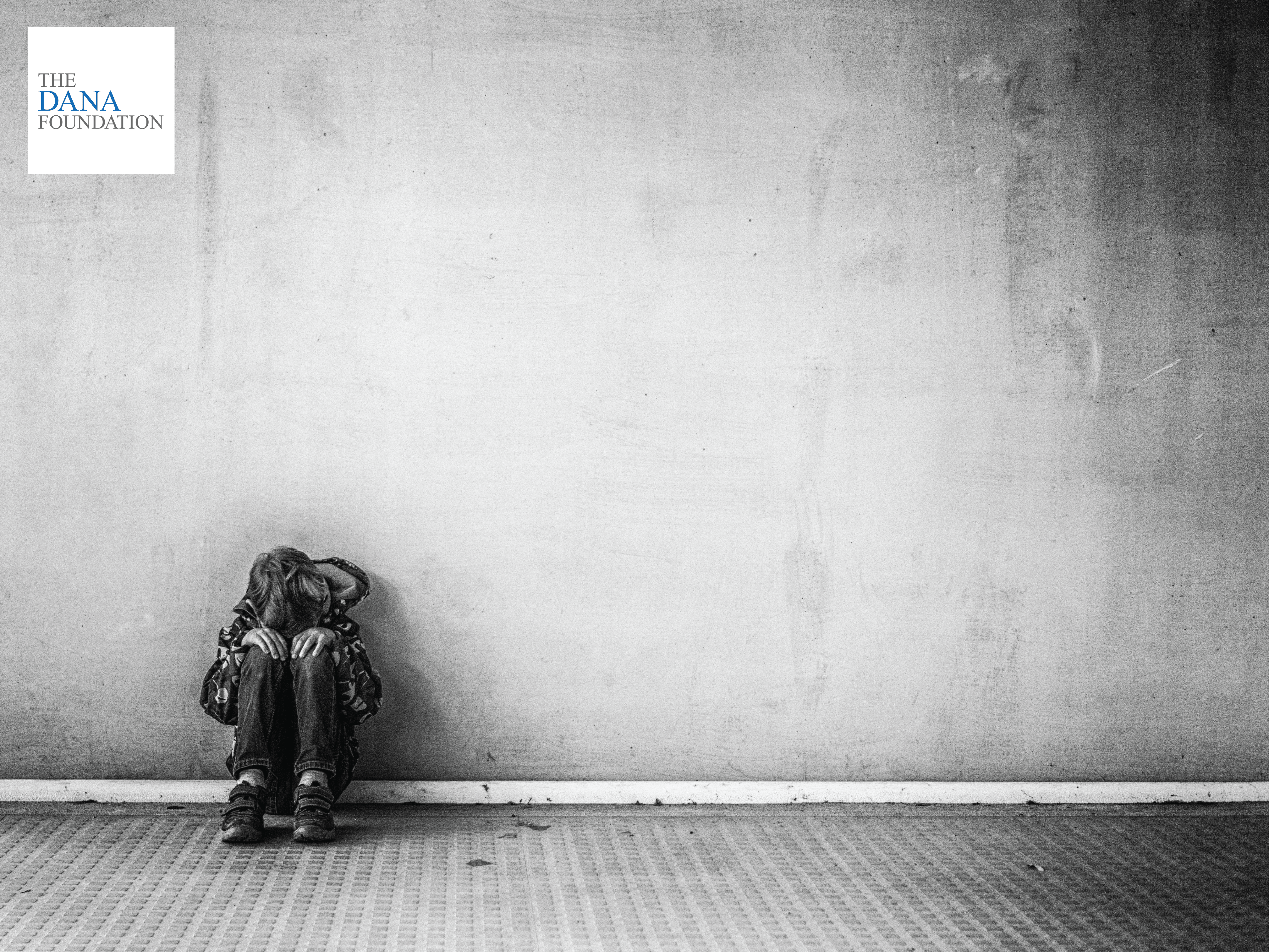 A small boy is crouched down in front of gray wall